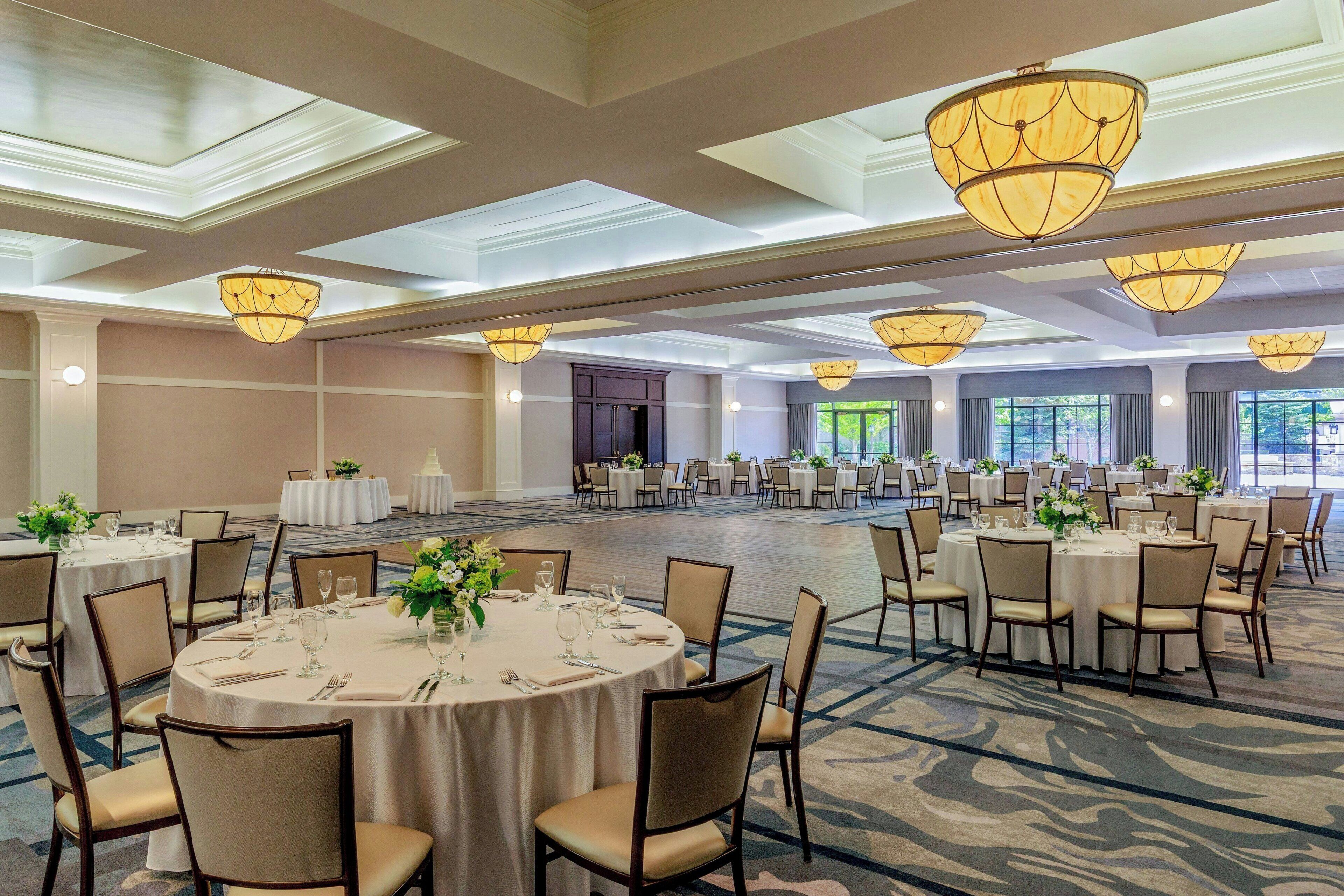 A large banquet hall with round tables, chairs, and hanging chandeliers.
