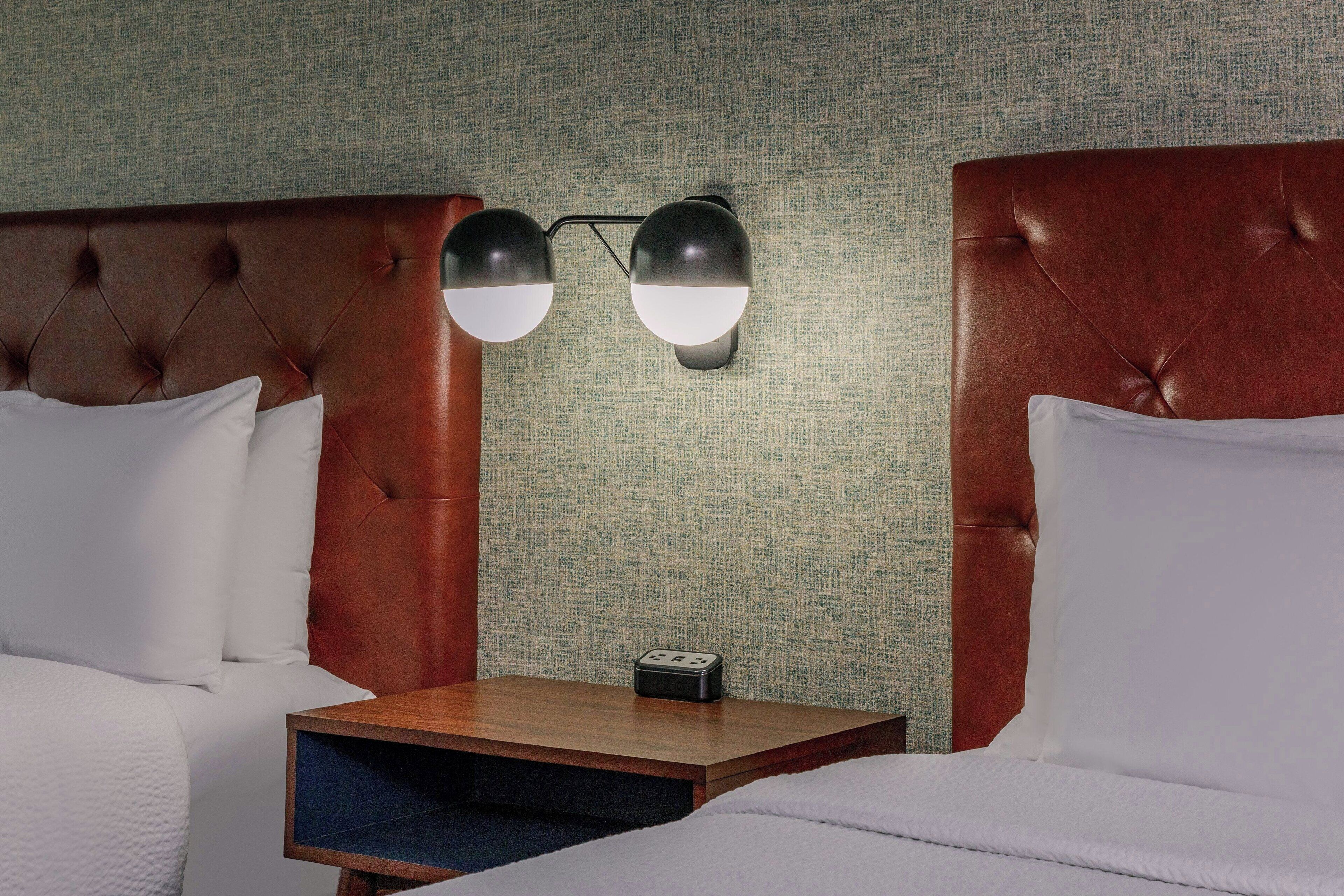 Habitación de hotel con un cabecero capitonado, dos mesitas de noche con lámparas y una pared con textura.