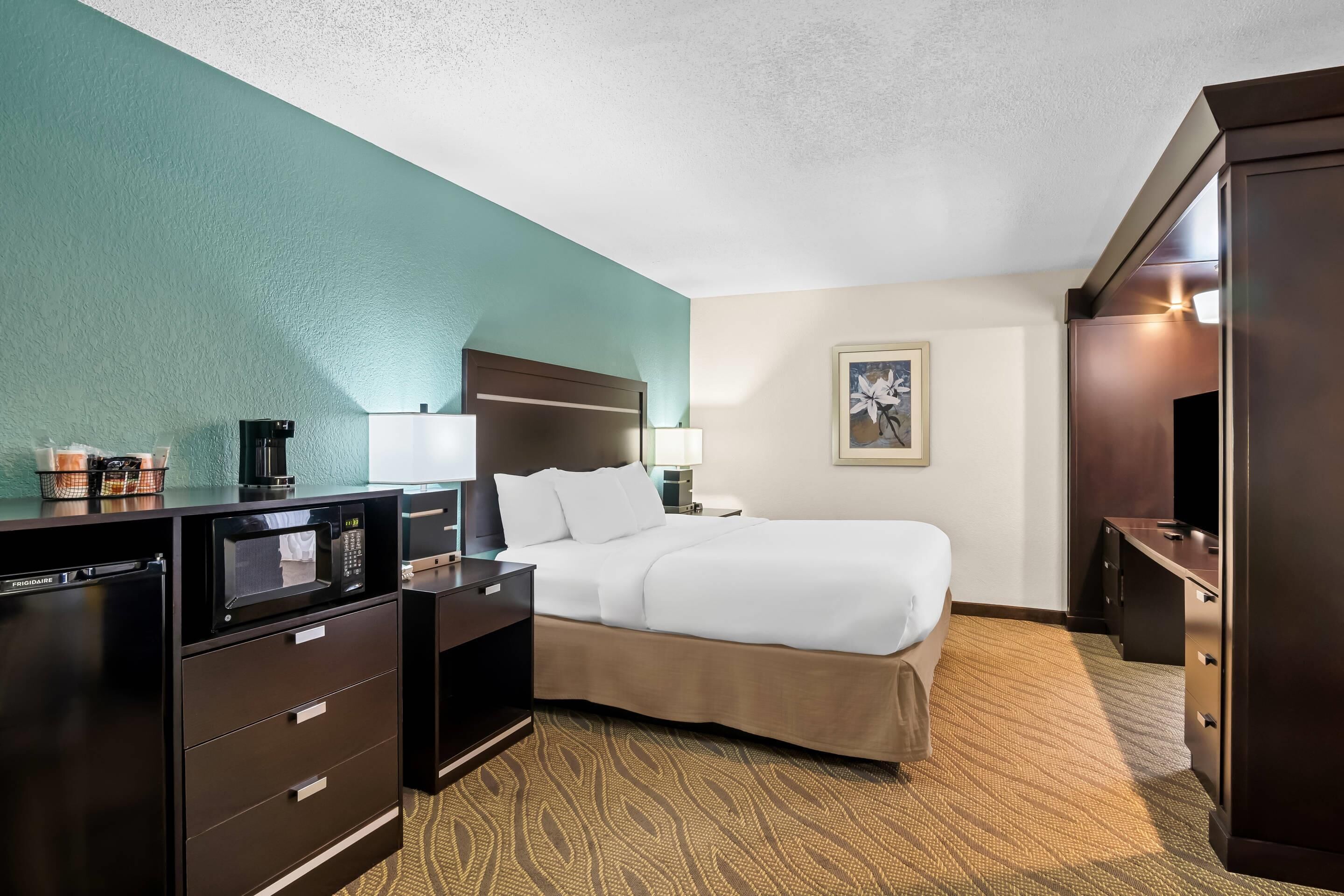 A hotel room with a bed, a desk with a microwave, a coffee maker, and a TV.