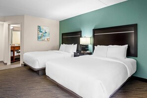 A hotel room with two beds, a painting on the wall, and a nightstand with a lamp.
