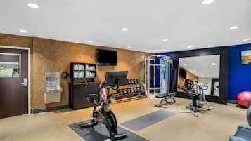 Une salle de sport moderne équipée de machines de cardio, d’haltères et d’un distributeur d’eau.