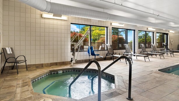 An indoor swimming pool with tiled walls, large windows, and lounge chairs.