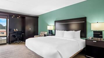 A hotel room with a large bed, a desk, and a chair. There are two lamps on the nightstands.