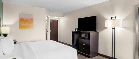 A hotel room with a bed, a flat-screen TV, a desk with a lamp, a microwave, and a small refrigerator.