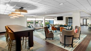 A spacious lobby with a long table, multiple chairs, sofas, and a patterned rug.