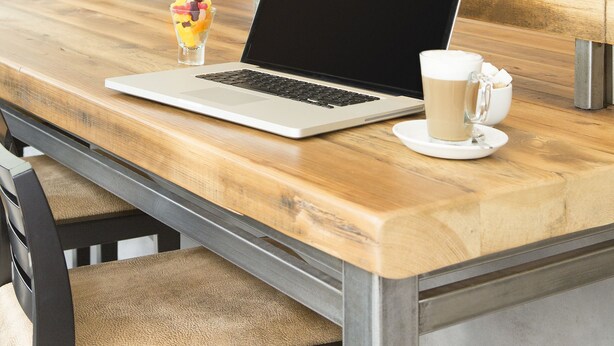 Ein Holztisch mit einem Laptop, einer Kaffeetasse und einem Dessert.