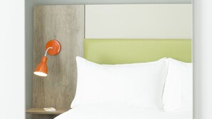 Ein Bett mit Holz-Kopfteil, einem weißen Kopfkissen und einer kleinen orangefarbenen Lampe.