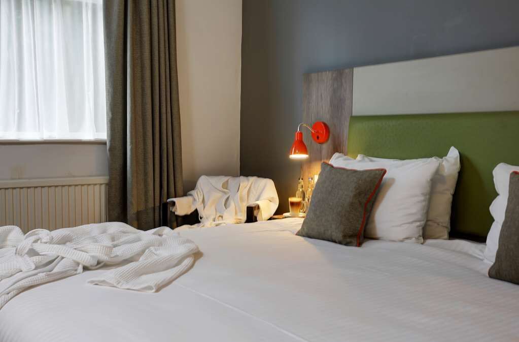 A hotel room with a large bed, white bedding, a green headboard, and a red wall-mounted lamp.