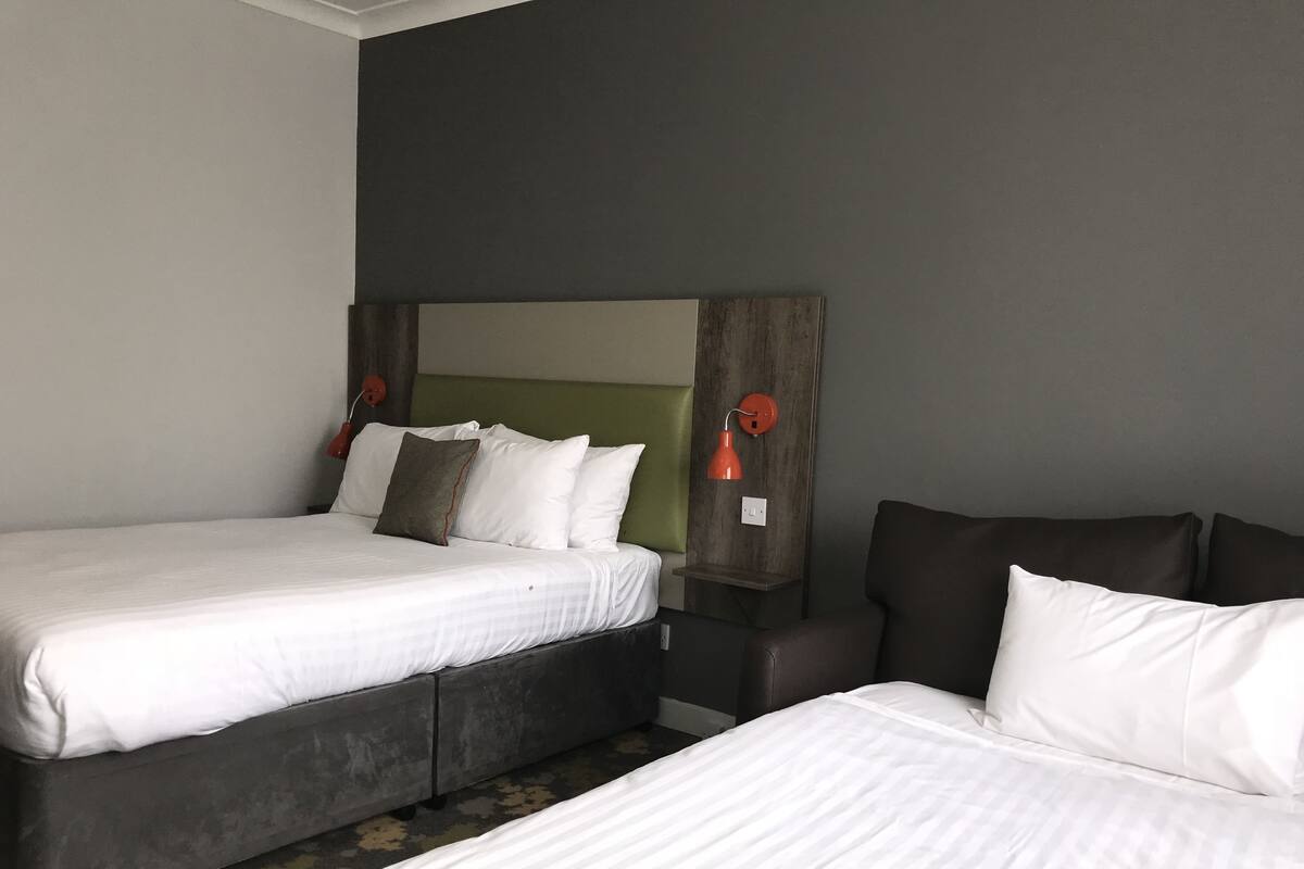 A hotel room with two beds, a large mirror, and two red wall lamps.