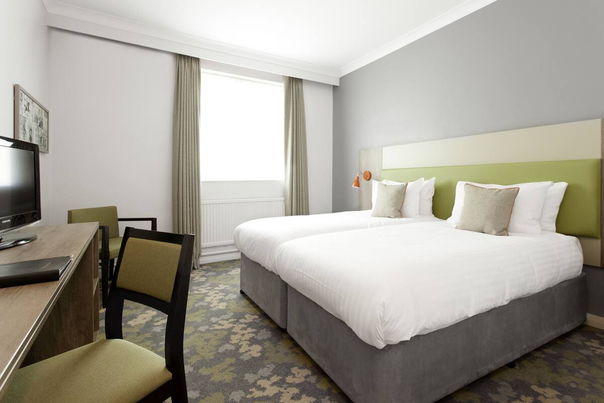 A hotel room with a large bed, a desk with a chair, a television, and a window with curtains.