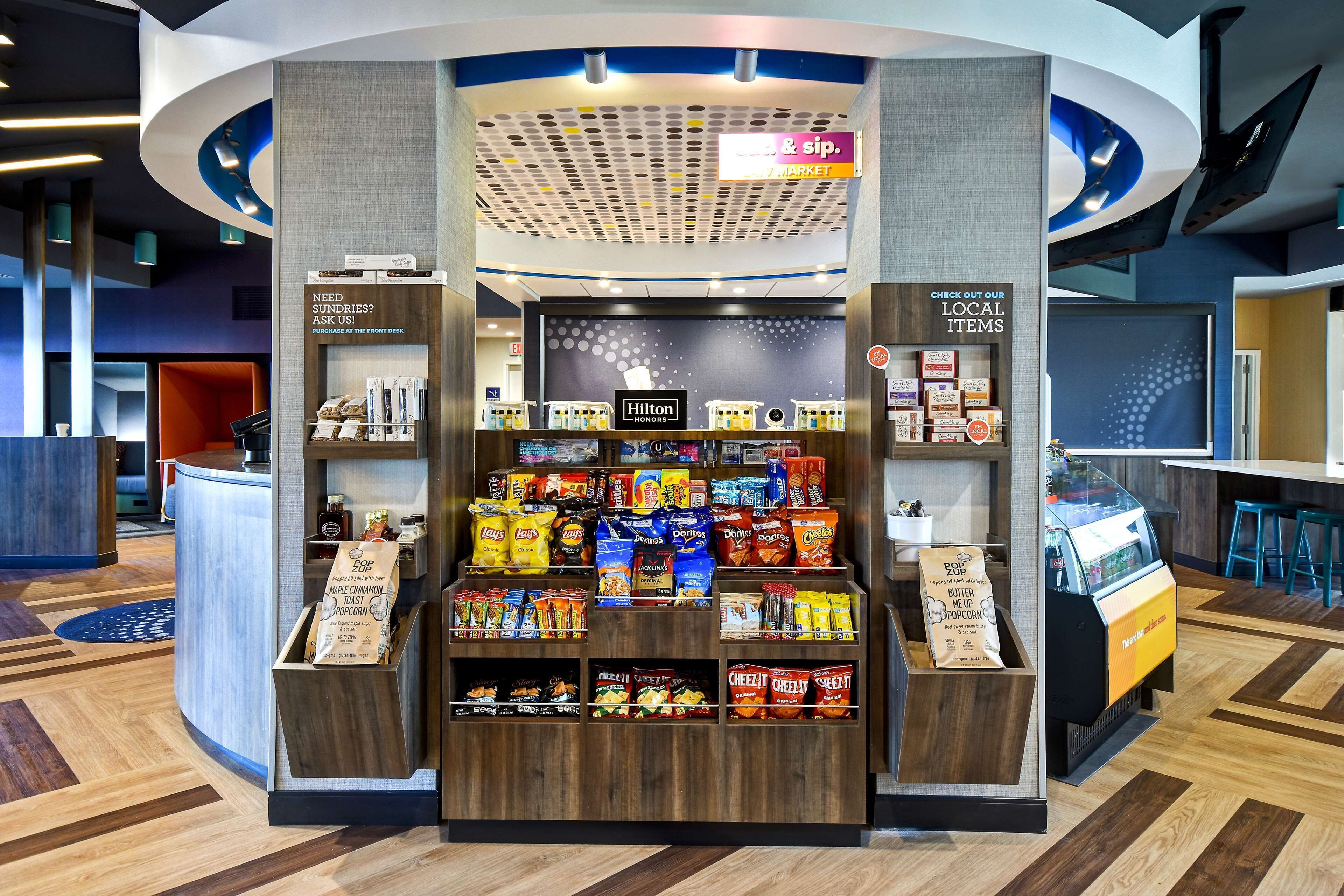A self-service kiosk with snacks and beverages, a Hilton Honors sign, and a 'Check Out Our Local Items' sign.