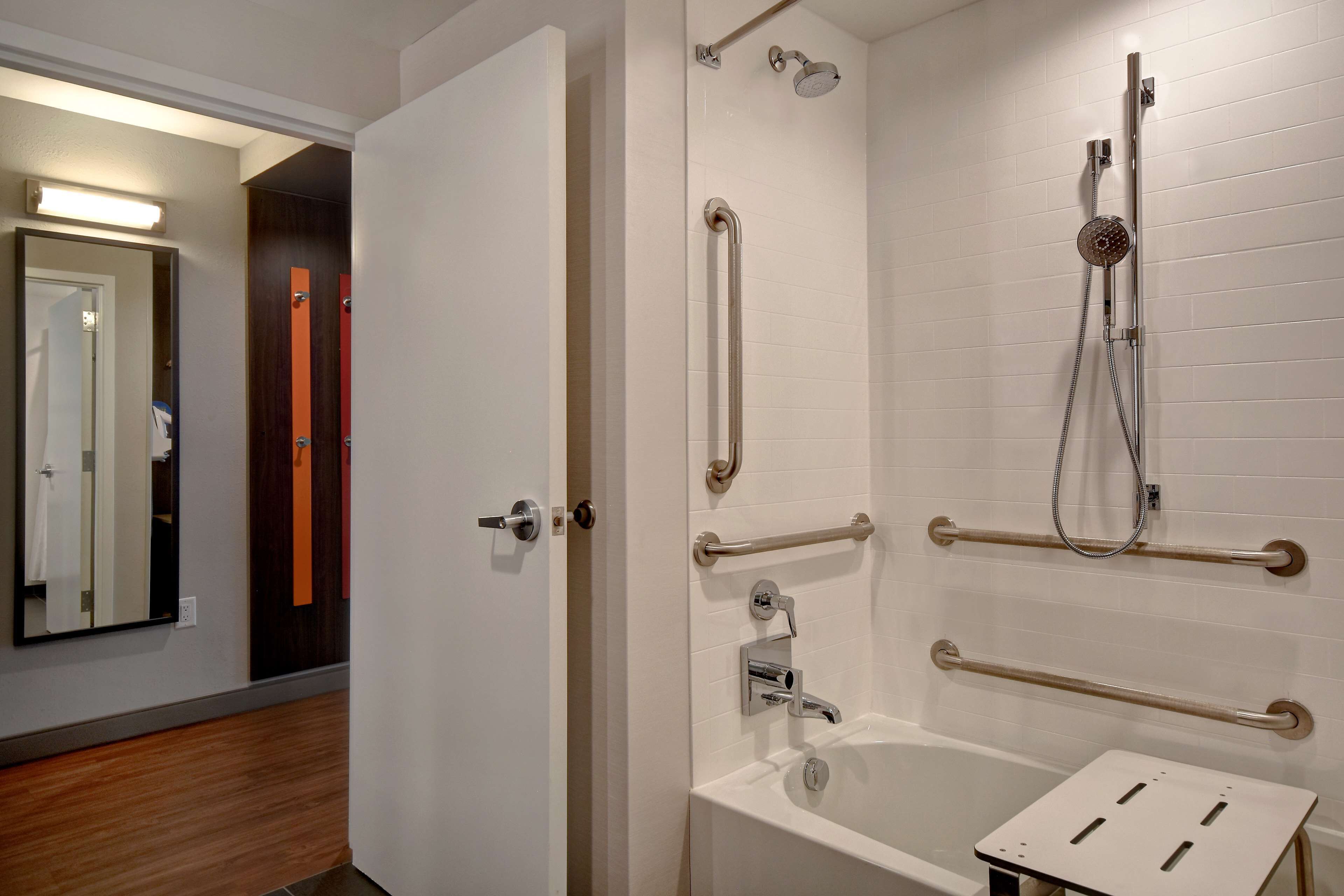 A bathroom with a white bathtub, grab bars, and a shower with a handheld showerhead.