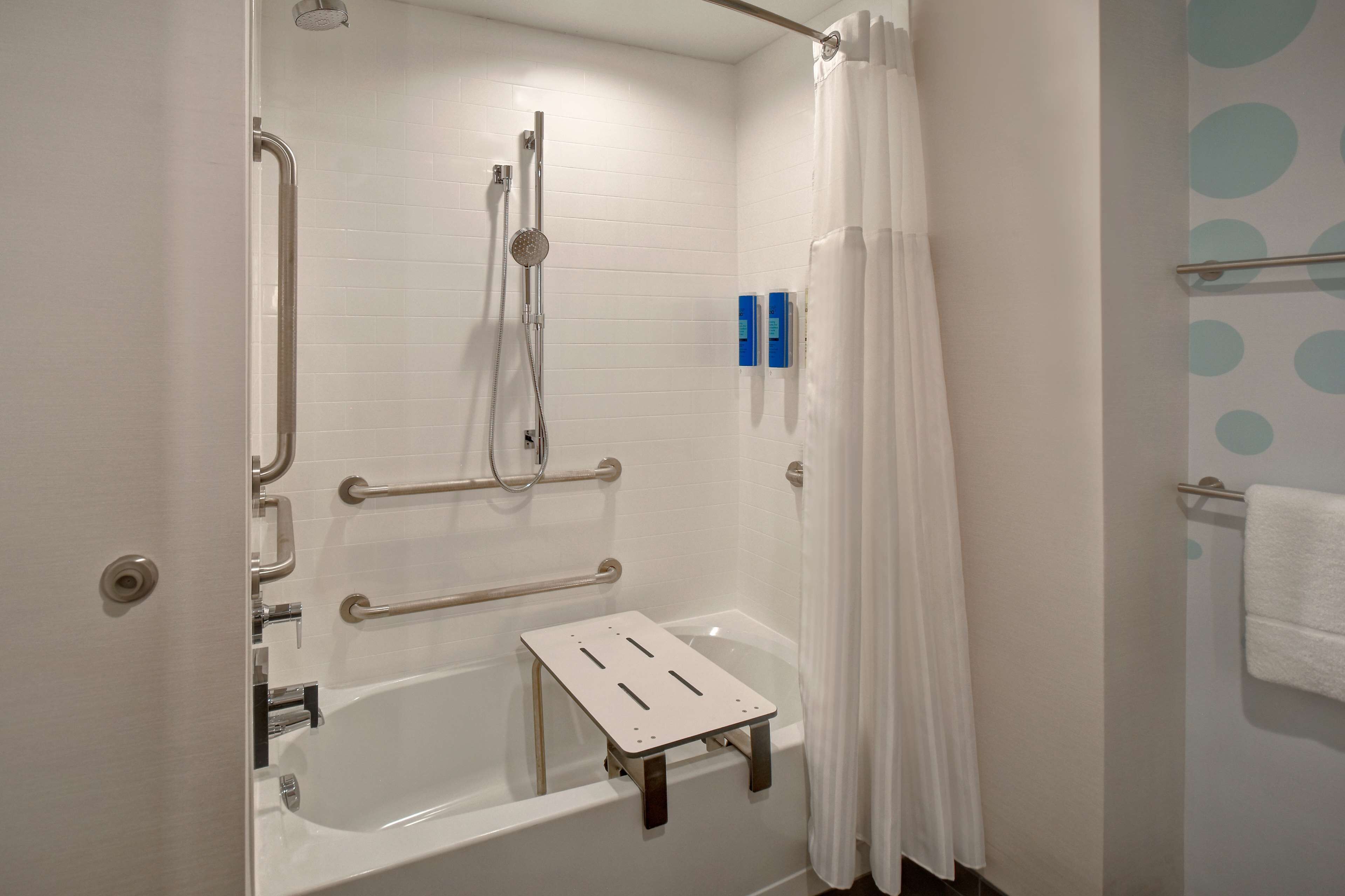 A walk-in shower with a grab bar, a handheld showerhead, and a white shower curtain.