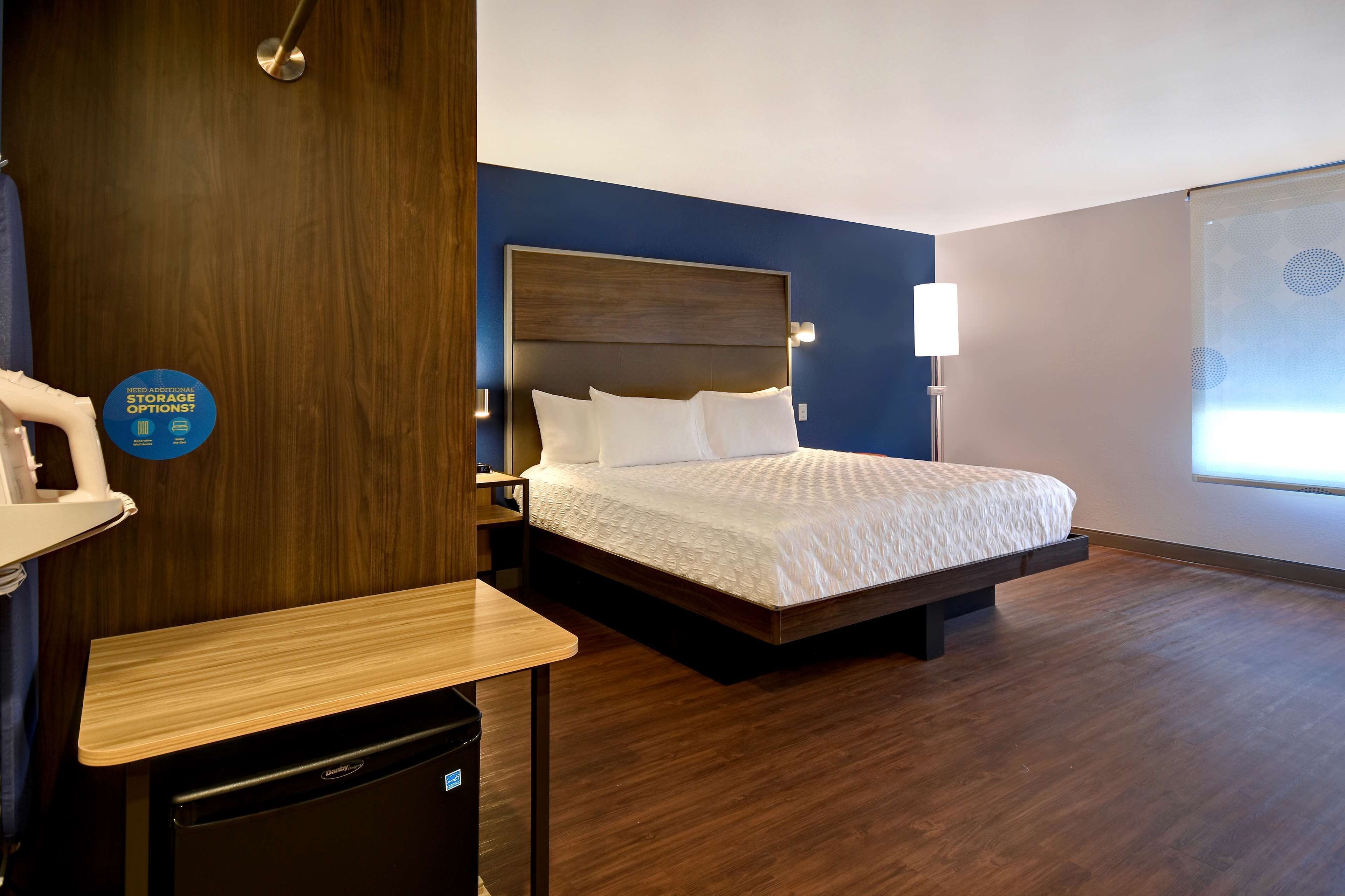 Una moderna camera d'albergo con pavimento in legno, un letto con biancheria bianca, una scrivania con una sedia e un comodino.