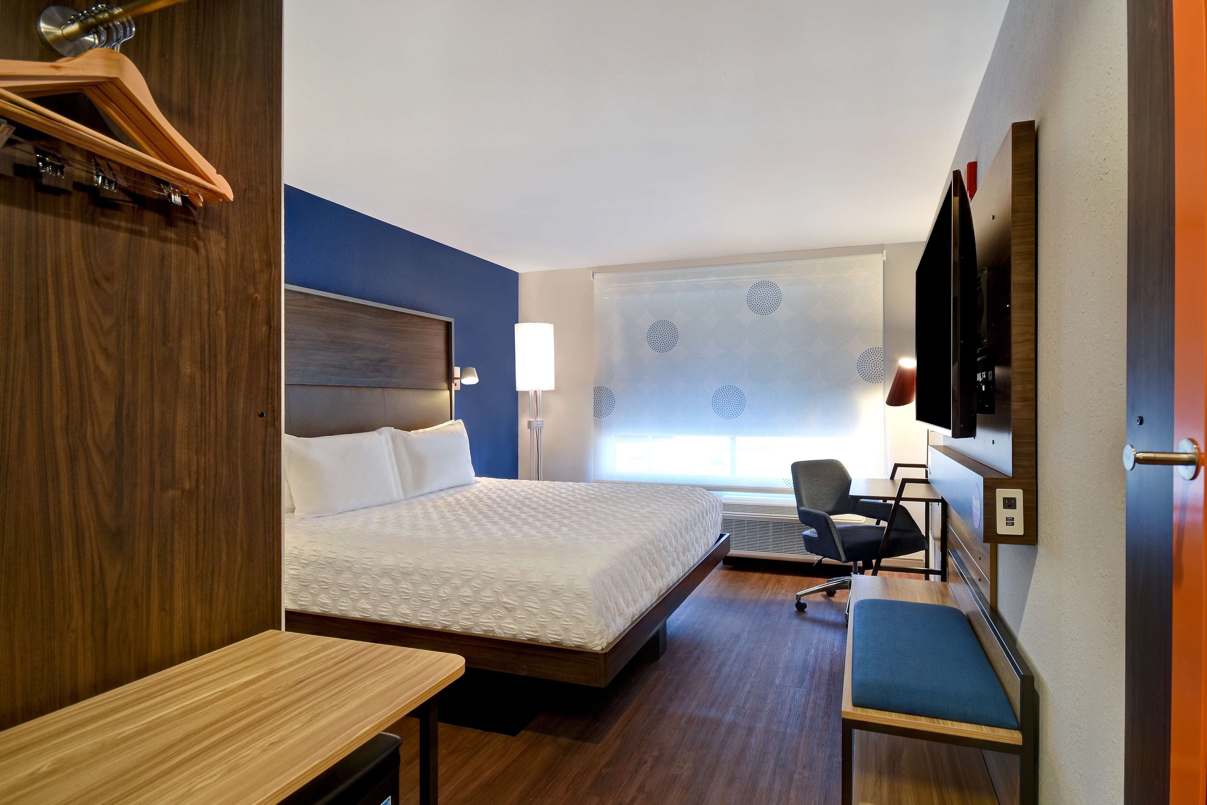 A hotel room with a bed, a desk, a chair, a TV, and a window with blinds.