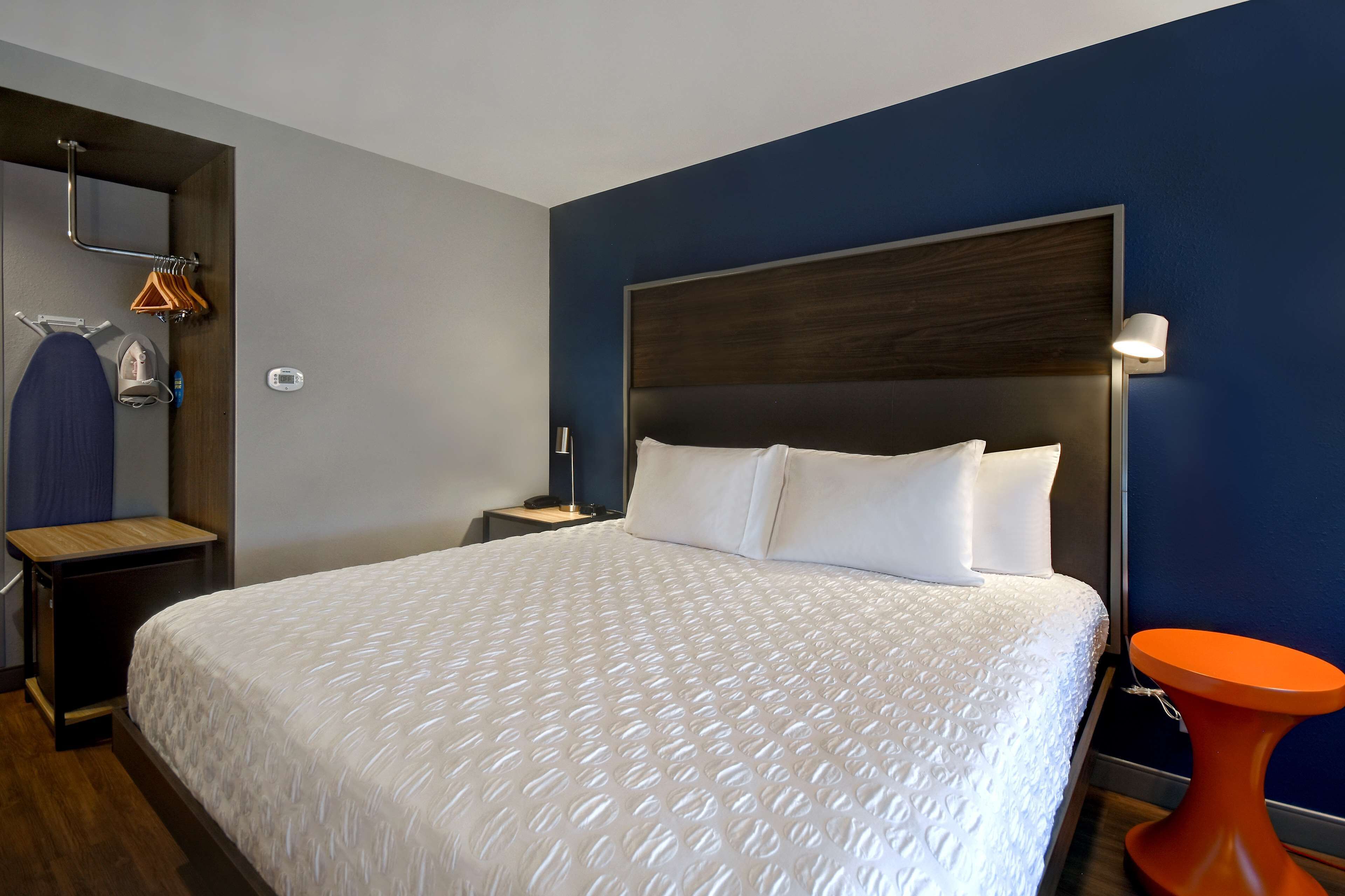 Una habitación de hotel con una cama grande, una mesita de noche, una lámpara de pared y una pequeña mesa naranja.