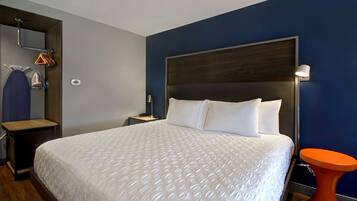 Una habitación de hotel con una cama grande, una mesita de noche, una lámpara de pared y una pequeña mesa naranja.