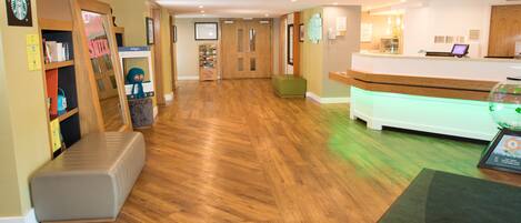 Un área de recepción con suelo de madera, un mostrador y un banco acolchado verde.