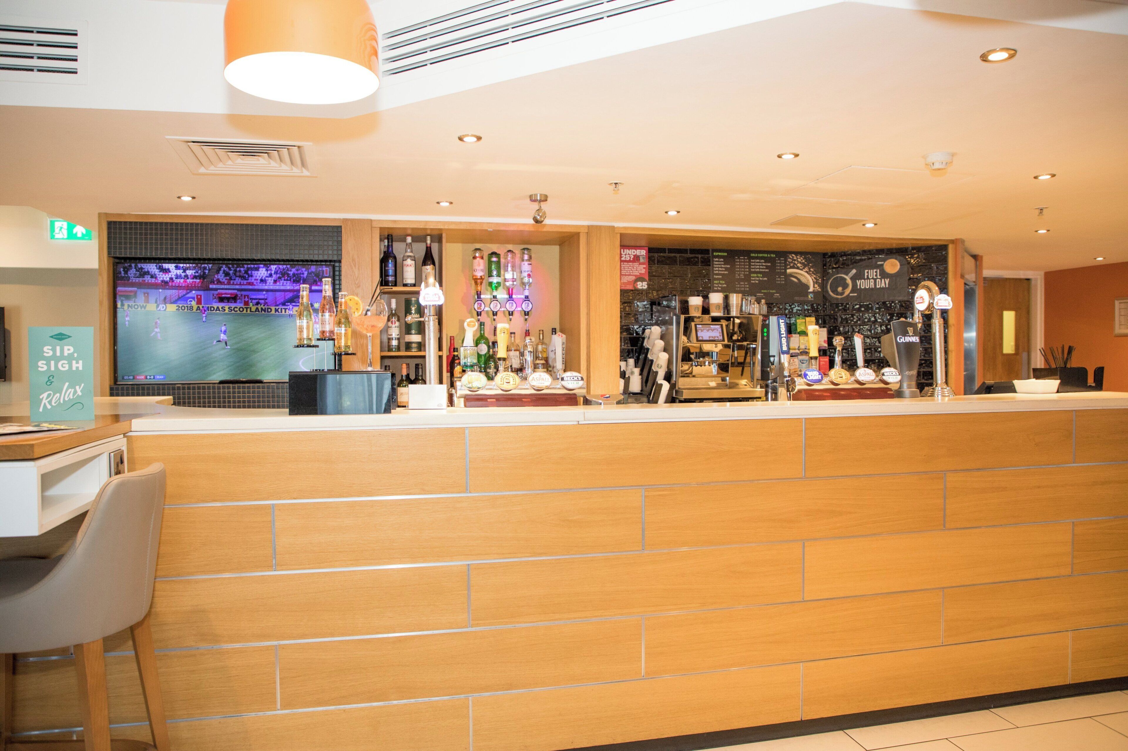 A bar area with a counter, shelves of bottles, and a television screen displaying a sports event.