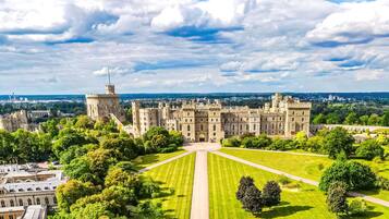 A large castle with a central courtyard, surrounded by lush greenery and a clear sky.