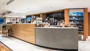 Zona bar moderna con bancone in legno, schienale piastrellato e area con sgabelli.