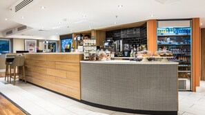 A modern bar area with a wooden counter, a tiled backsplash, and a seating area with stools.