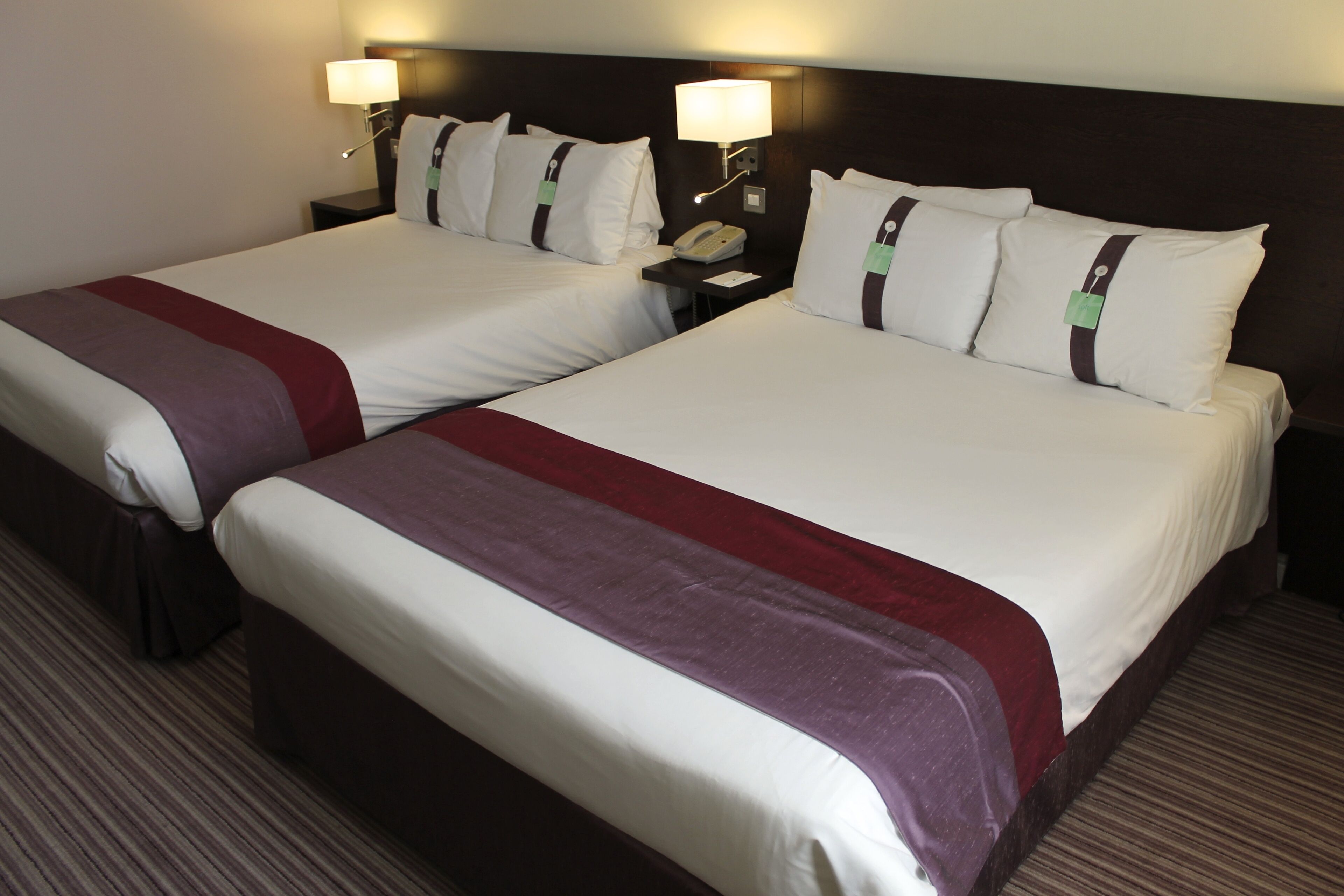 A hotel room with two beds, each with a red and white bedspread, a nightstand with a lamp, and a telephone.