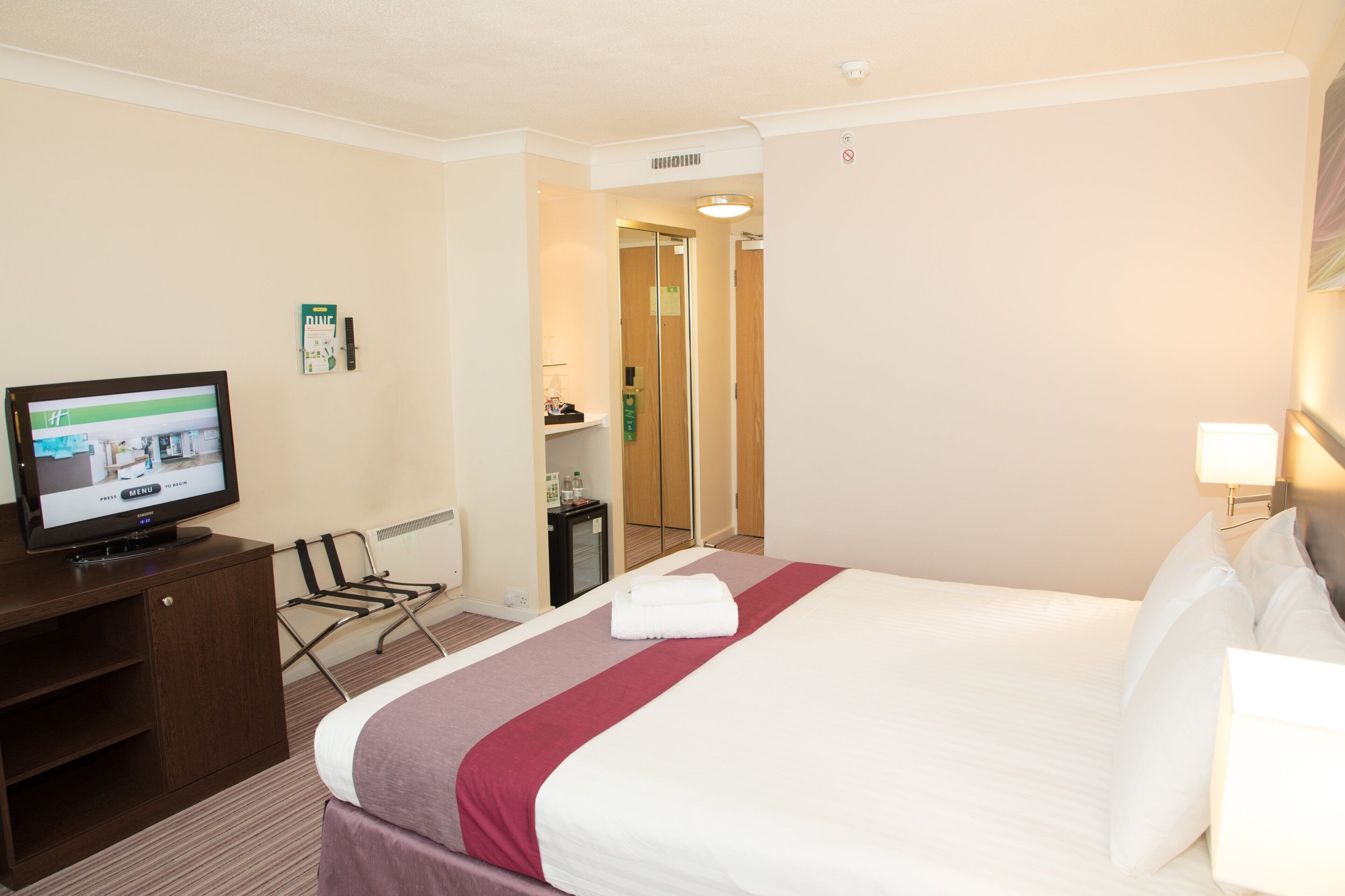 Ein Hotelzimmer mit Bett, Fernseher, Schreibtisch und Kleiderschrank.
