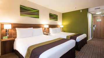 Habitación de hotel con dos camas, cabecero de madera, lámparas de noche y un cuadro abstracto de motivos verdes.