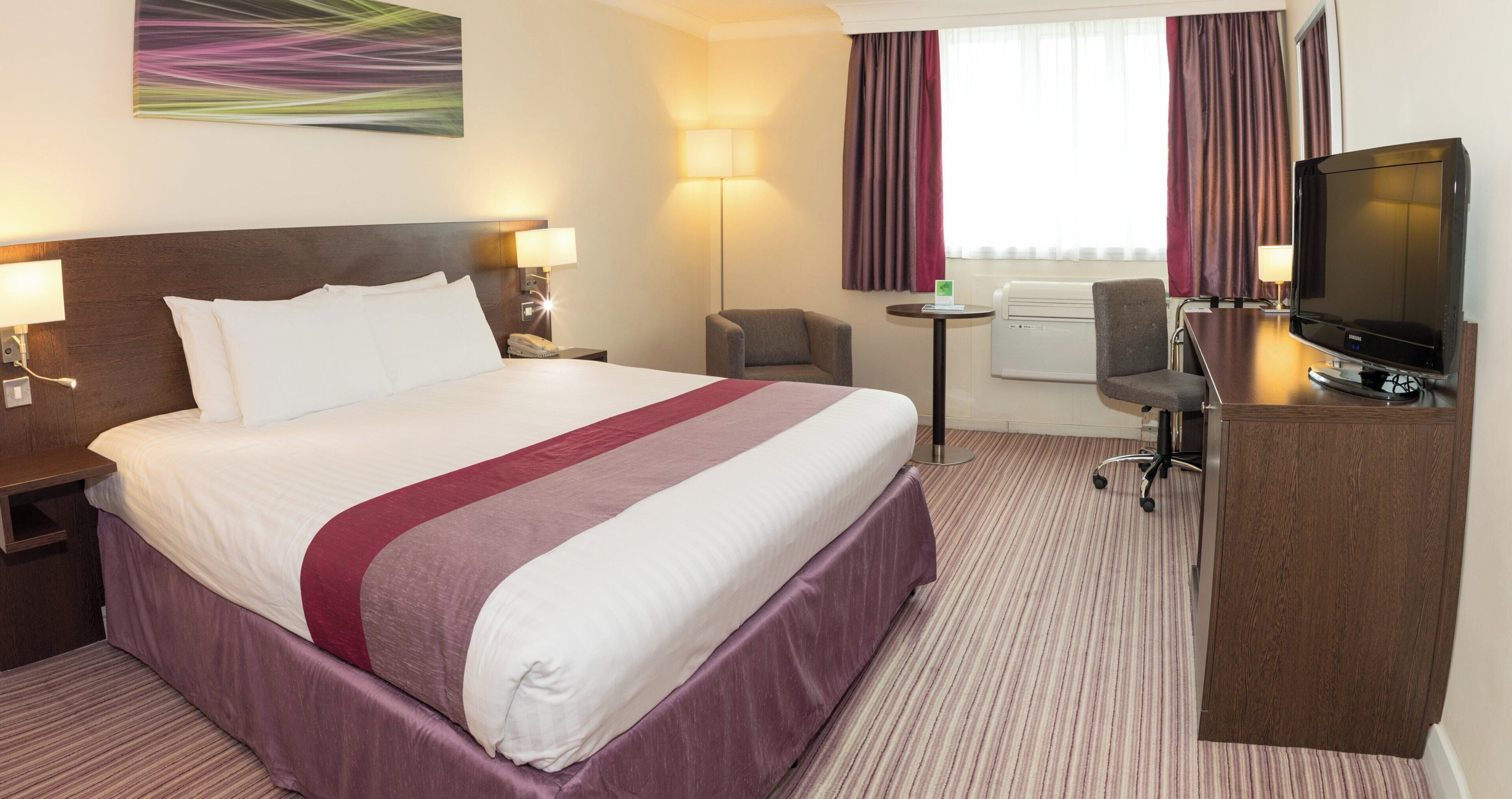 Een hotelkamer met een groot bed, een bureau met een televisie, een stoel en een bijzettafeltje.