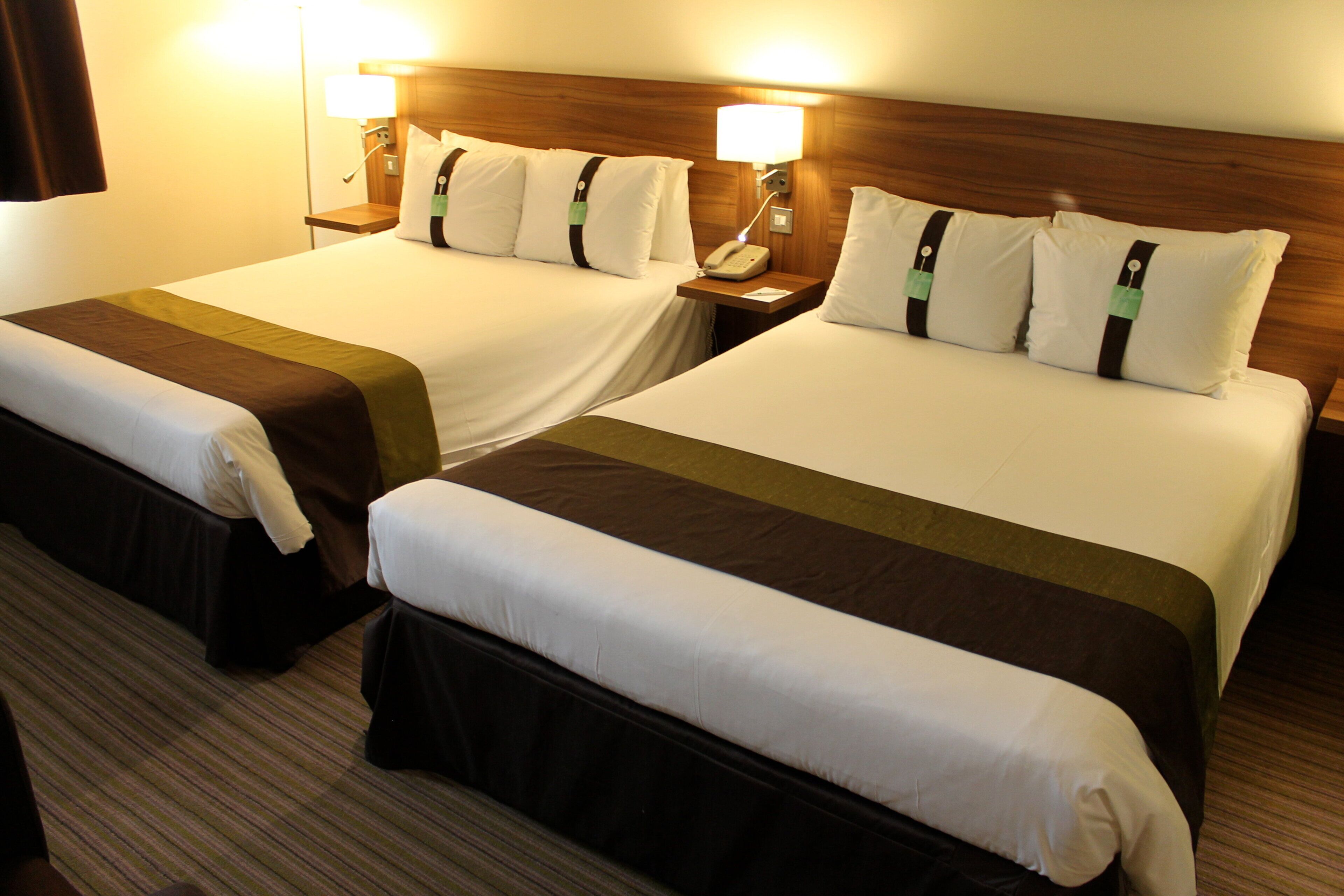 A hotel room with two beds, each with a wooden headboard, bedside lamps, and a telephone on the nightstand.