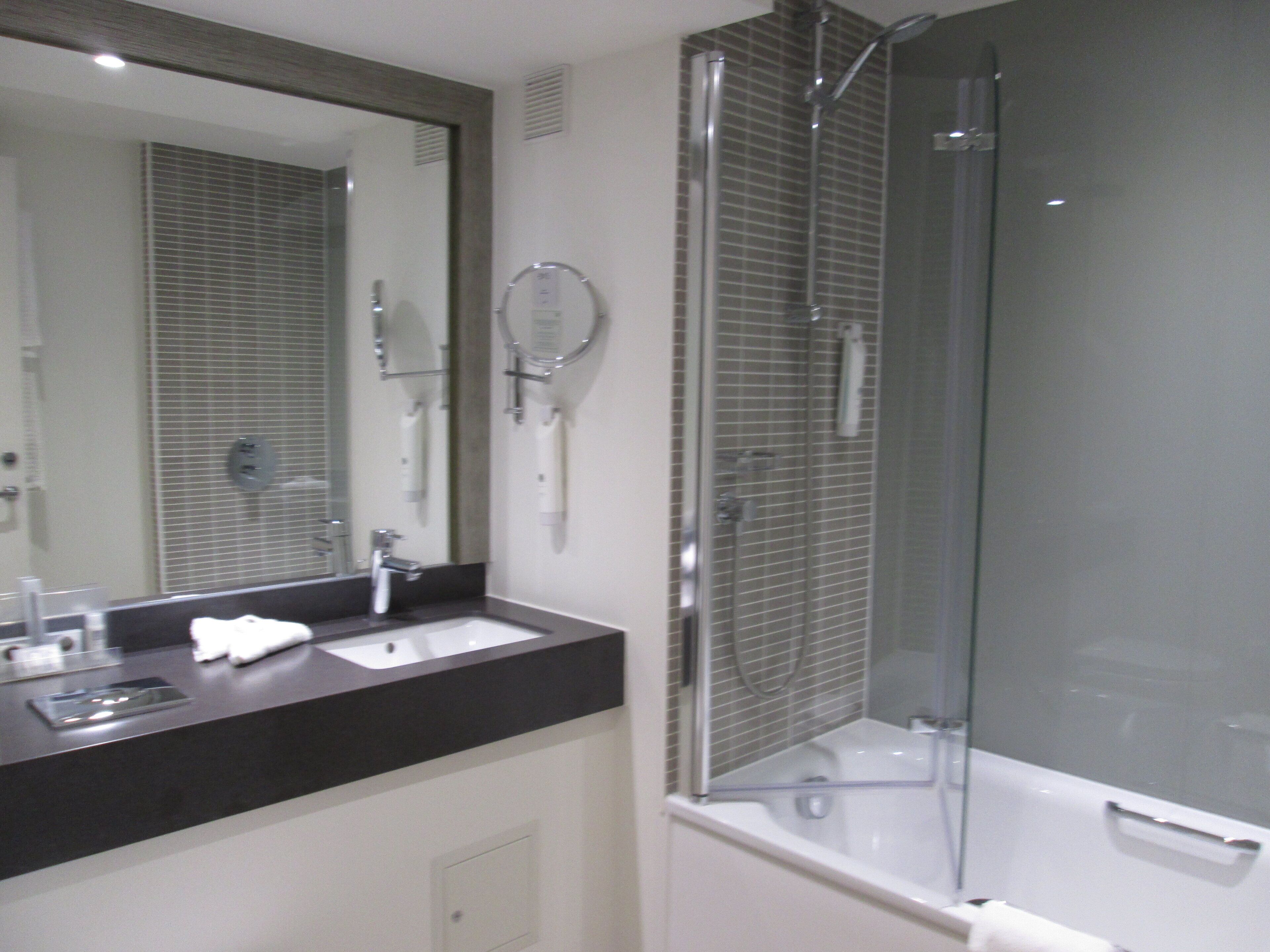 A modern bathroom with a large mirror, a sink, and a glass-enclosed shower.