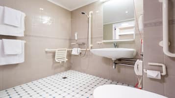 Un baño con lavamanos blanco, ducha e inodoro. Toallas blancas cuelgan de la pared.