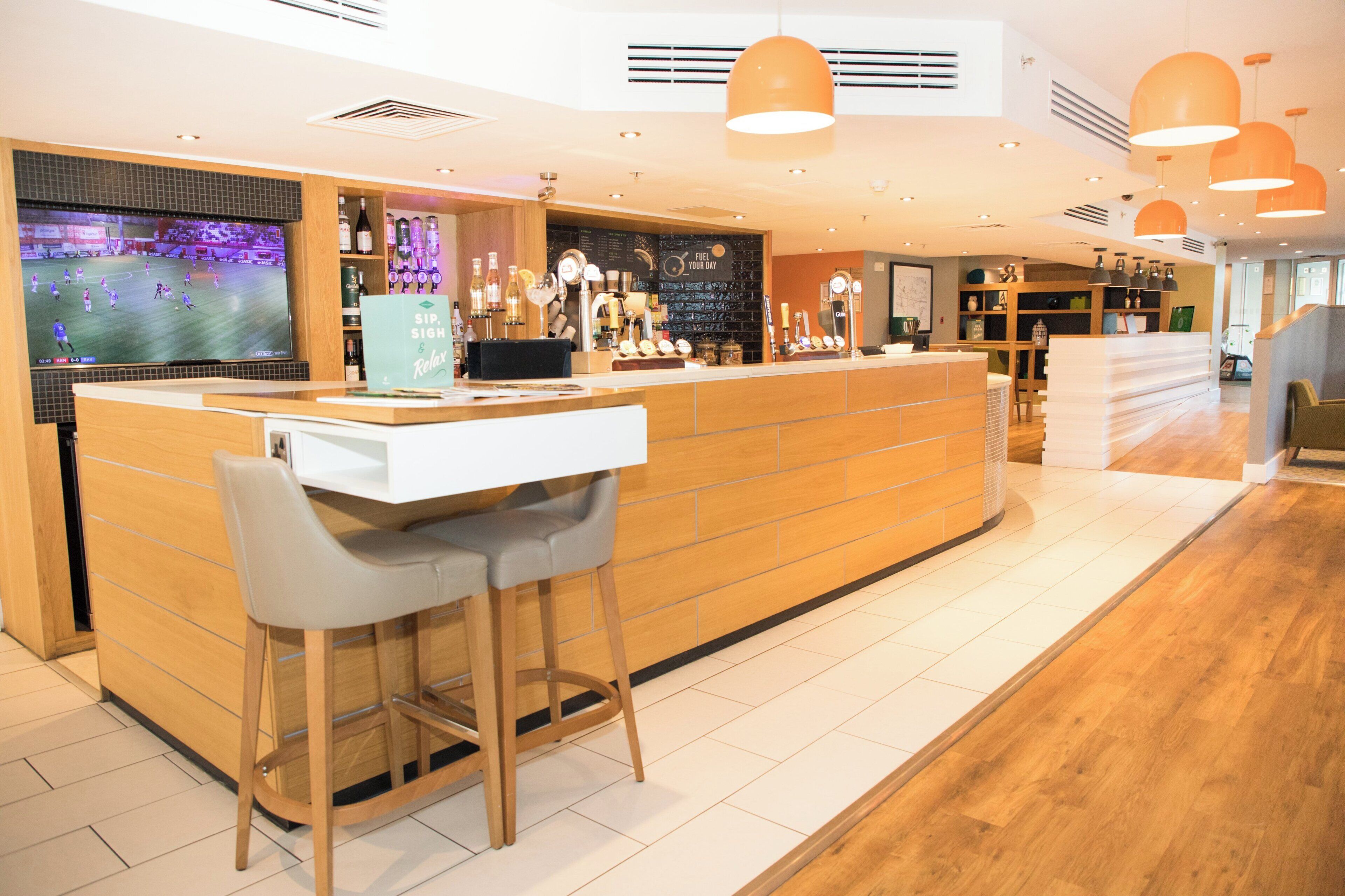A bar area with a counter, stools, and a television screen displaying a sports event.