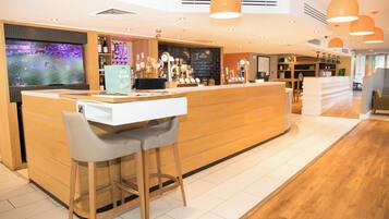 A bar area with a counter, stools, and a television screen displaying a sports event.