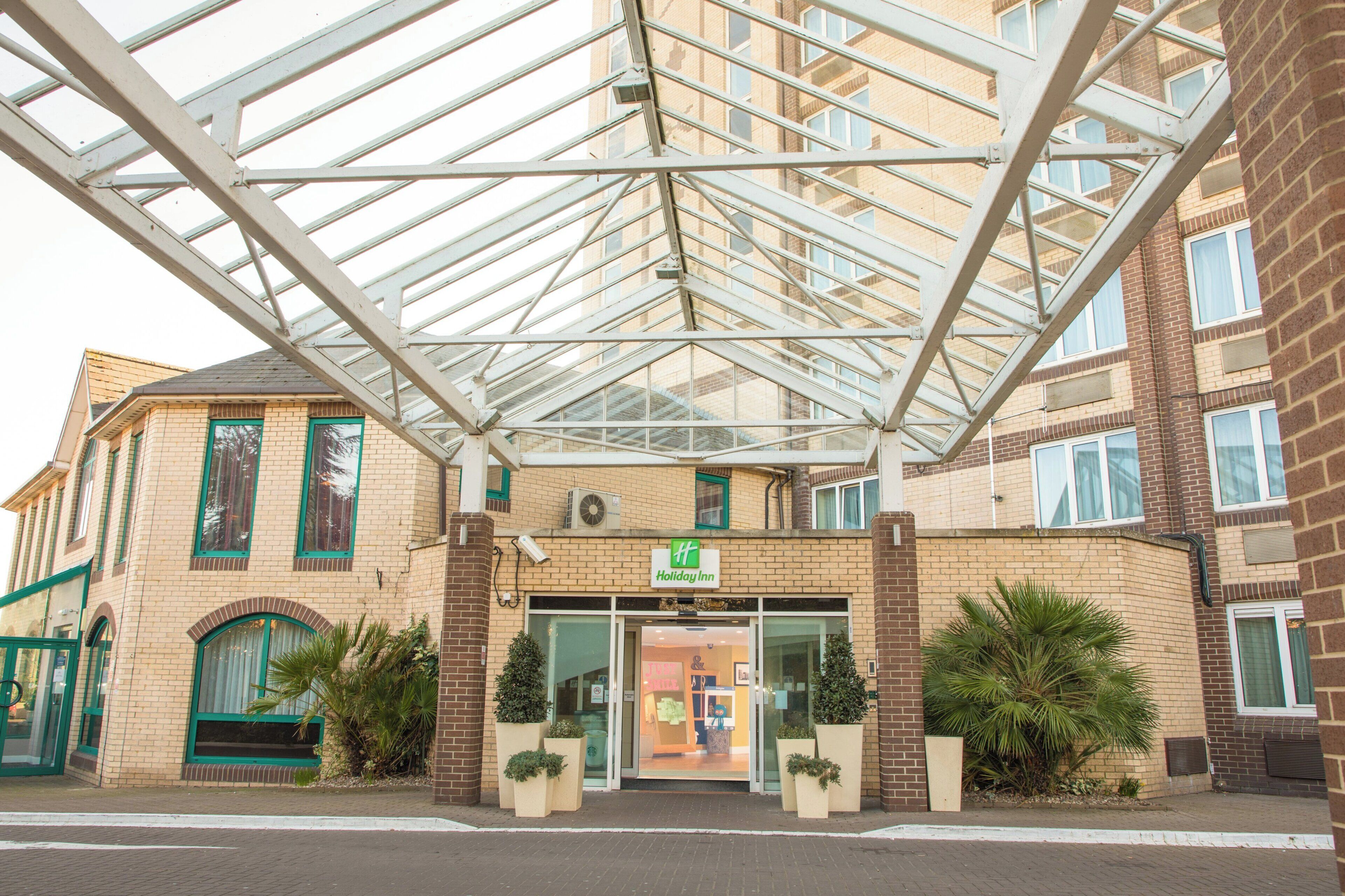 Un hotel con entrada cubierta de vidrio, fachada de ladrillo y plantas de exterior.