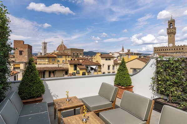 A rooftop terrace with outdoor seating, potted plants, and a view of historic buildings and a clock tower. - Gallery Hotel Art - Lungarno Collection (Florence)