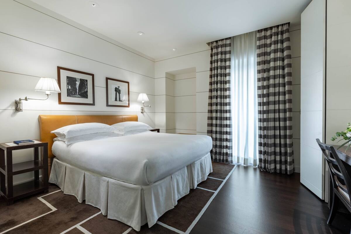 A hotel room with a large bed, two bedside lamps, a nightstand, a framed picture, and a checkered curtain.