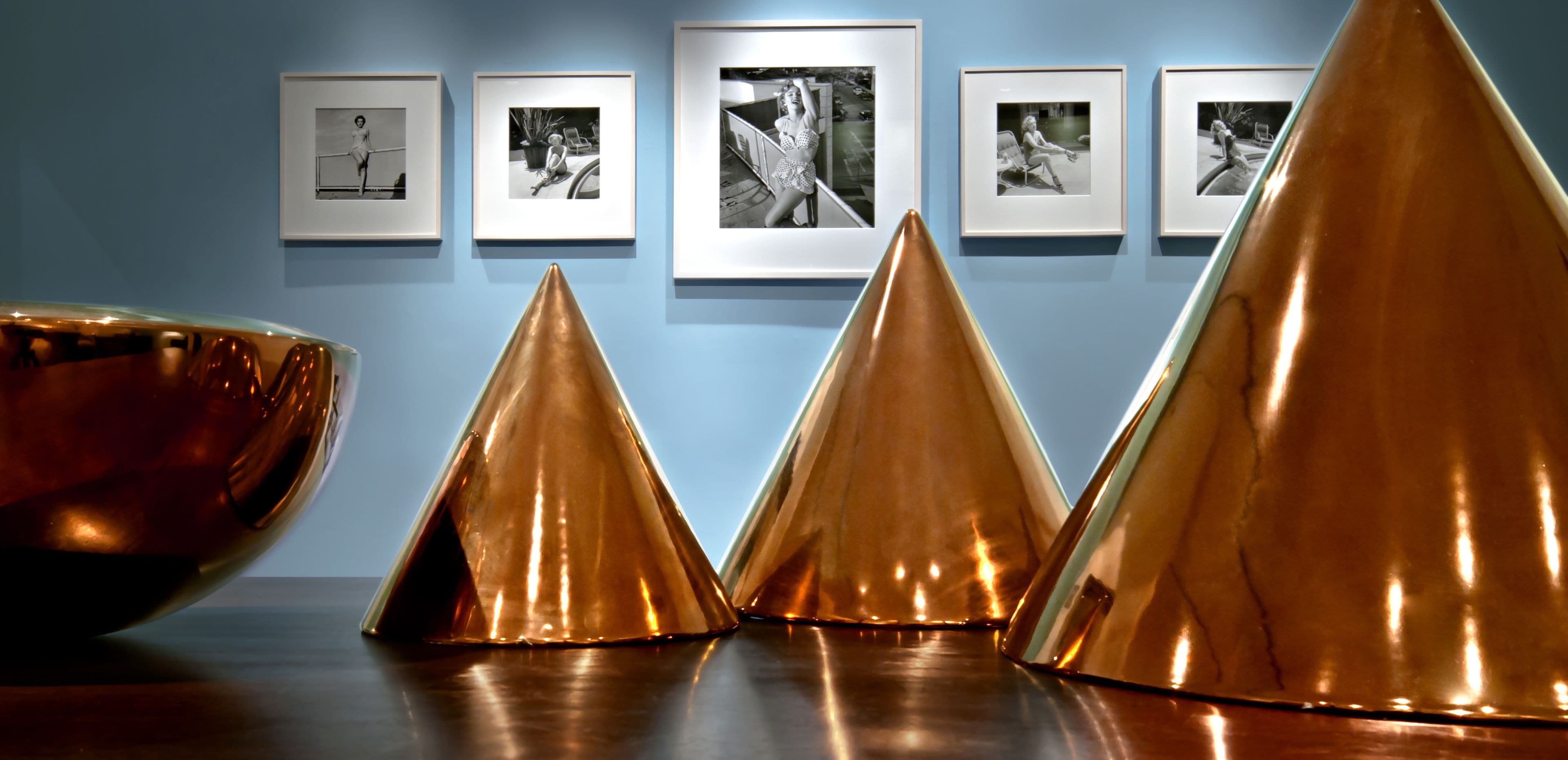 A room with a blue wall and framed photographs. There are three large, shiny, triangular objects on the floor.