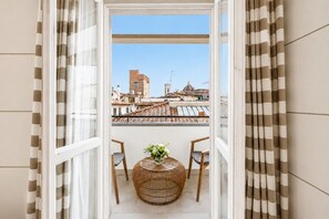 A balcony with a view of buildings, a wicker chair, and a small table with a vase. - Gallery Hotel Art - Lungarno Collection (Florence)