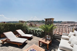 Une terrasse sur le toit, avec des chaises longues, une petite table et une vue sur le paysage urbain.