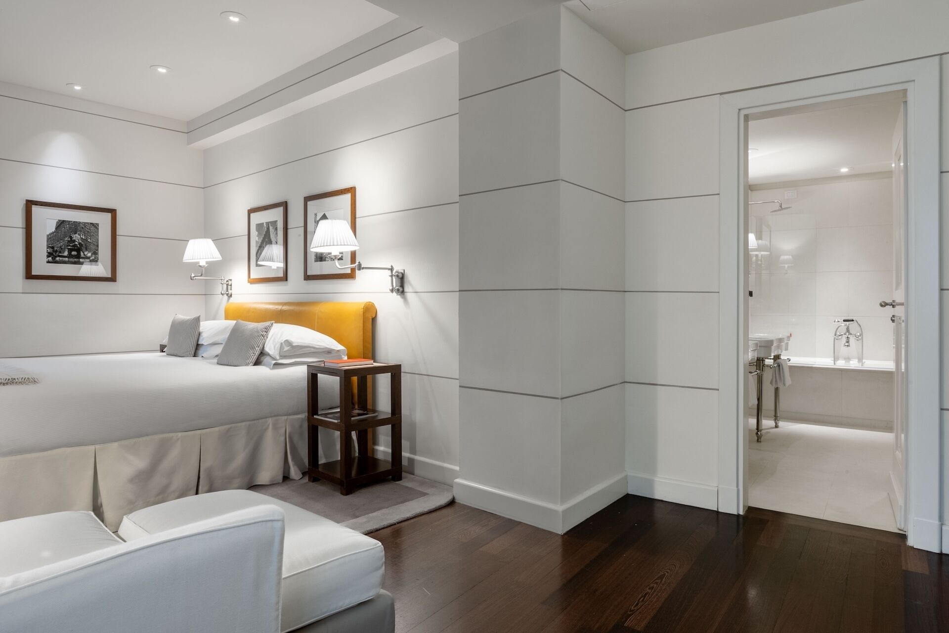 A modern hotel room with a bed, bedside table, and a bathroom visible through an open door.