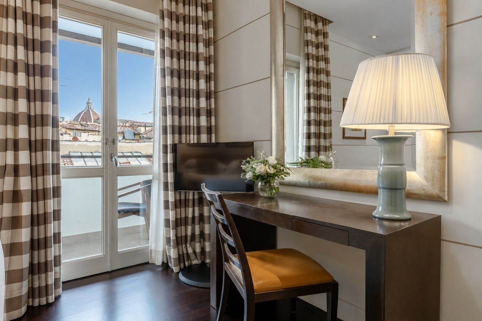 Une chambre d’hôtel équipée d’un bureau, d’une chaise, d’une lampe et offrant une vue sur le paysage urbain par la fenêtre.