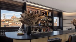 A bar with a view of a historic building, shelves of liquor bottles, and decorative plants. - Gallery Hotel Art - Lungarno Collection (Florence)