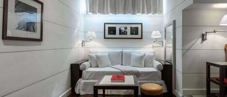 A modern hotel room with a sofa, a small table, a chair, a framed picture, and a window with curtains.
