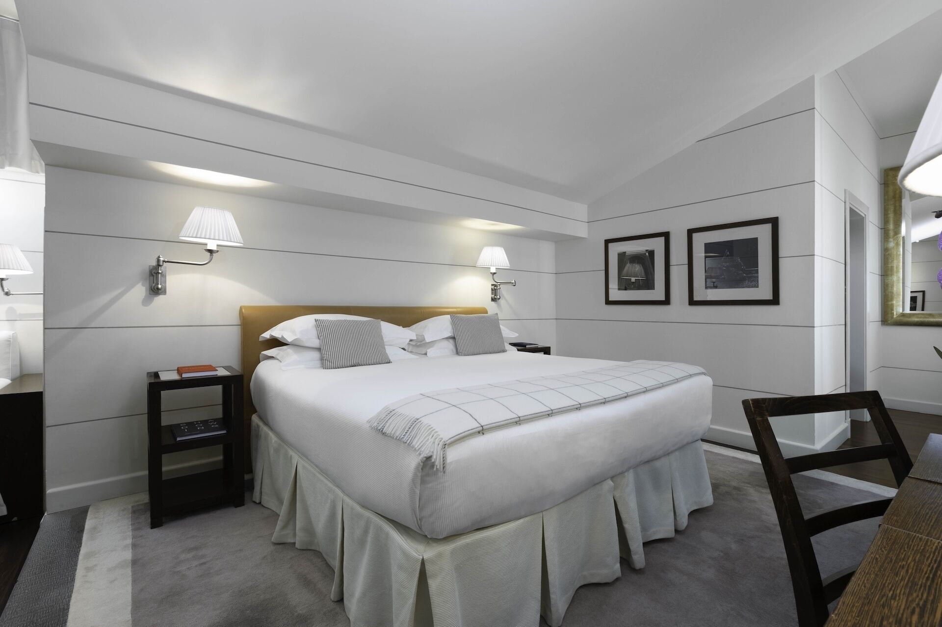 Moderni hotellihuone, jossa on suuri sänky, yöpöydät, seinään kiinnitetyt lamput ja kehystetyt taulut.
