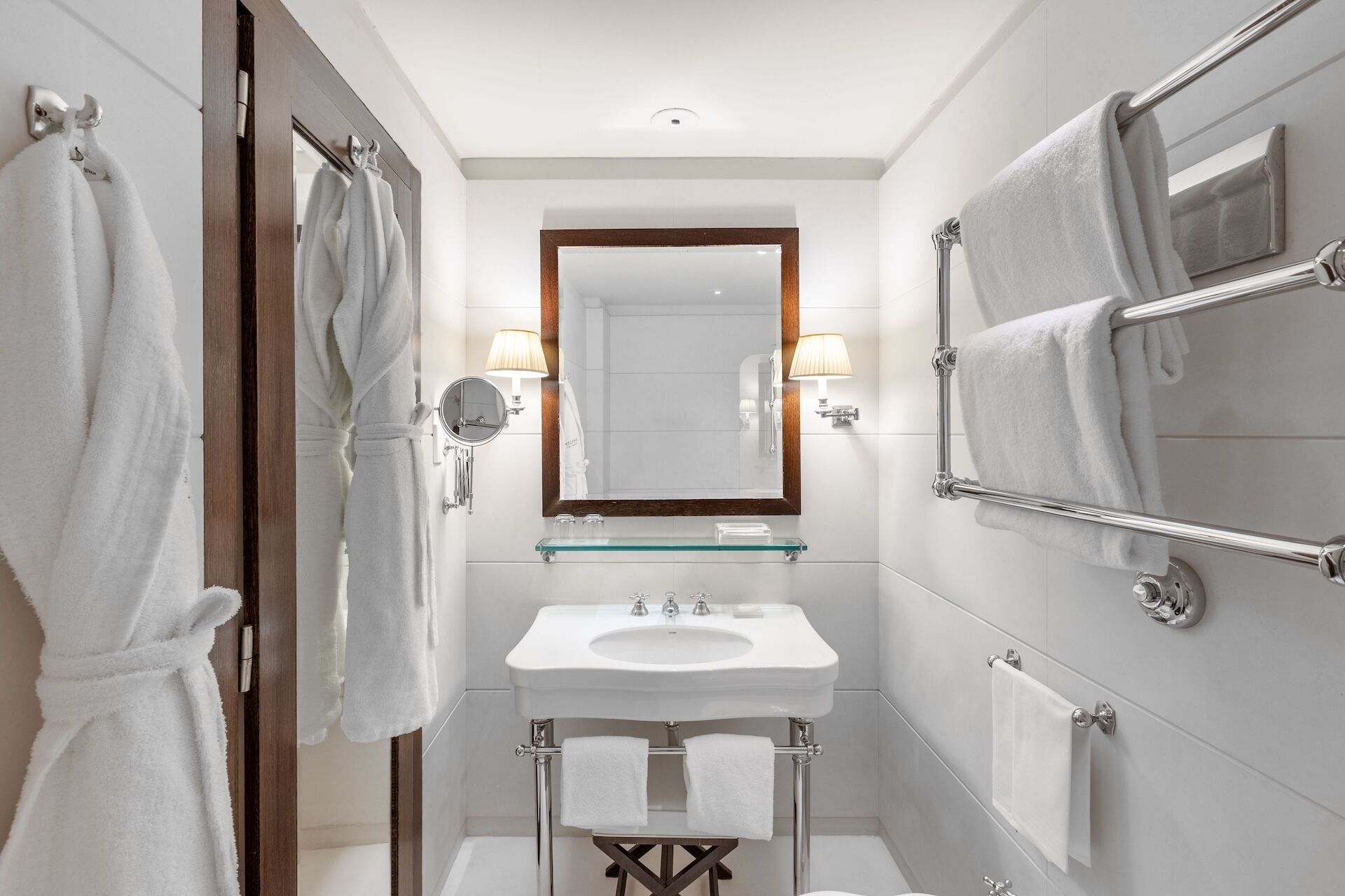 A modern bathroom with a glass sink, a large mirror, and multiple towel racks.