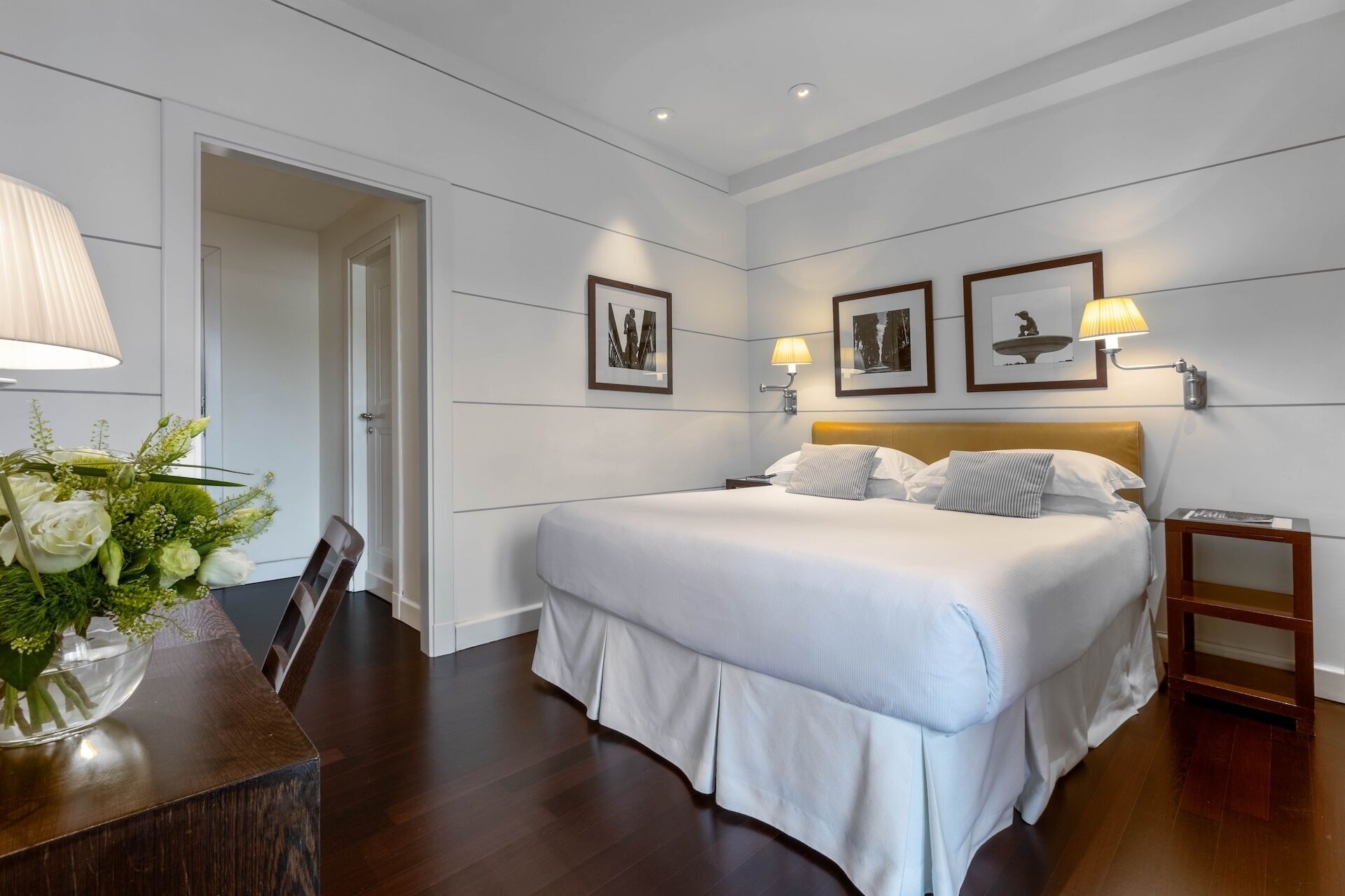 A hotel room with a large bed, bedside lamps, a wooden nightstand, and framed pictures on the wall.