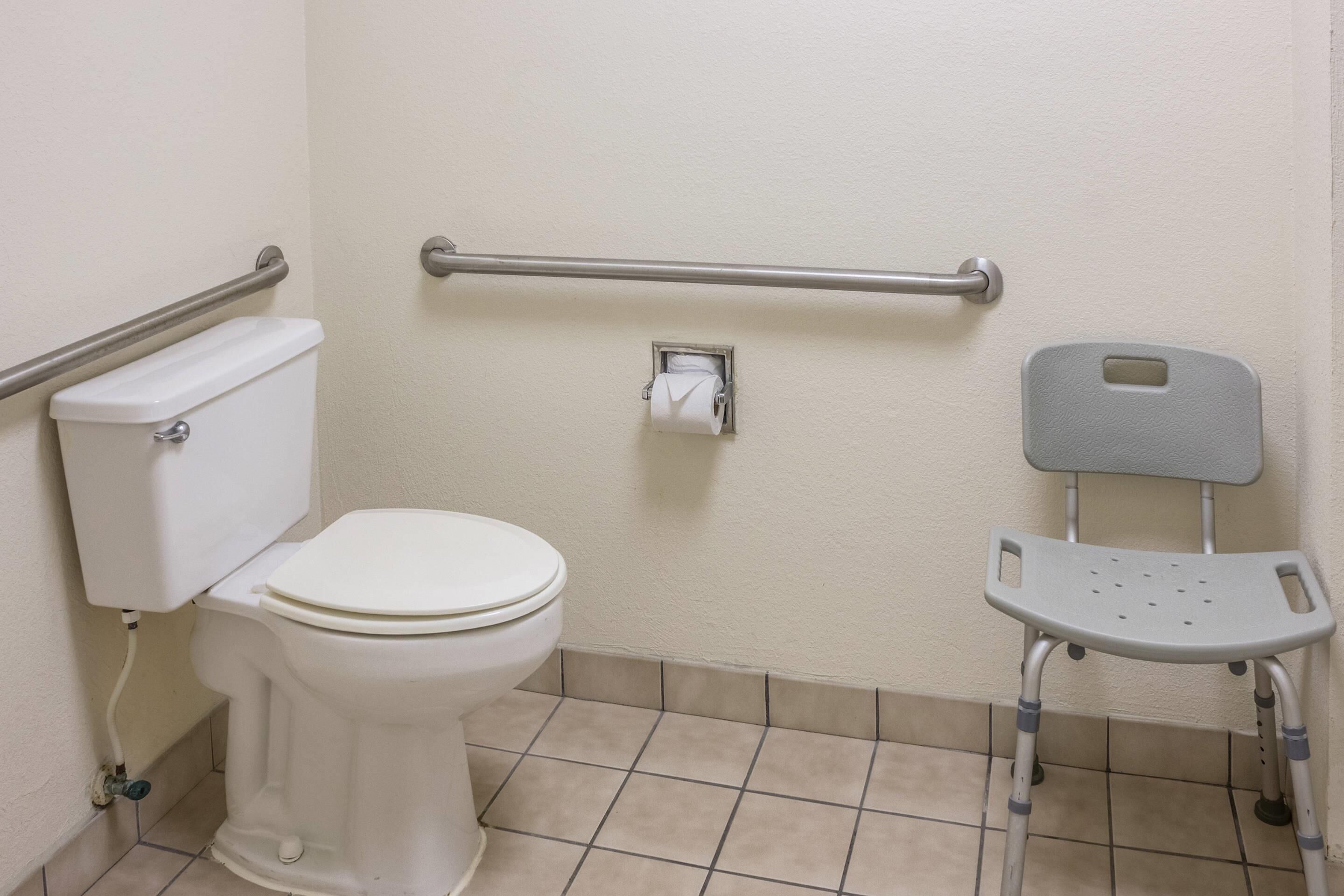 Un baño con inodoro, barra de apoyo, barra de sujeción y banco accesible para sillas de ruedas.