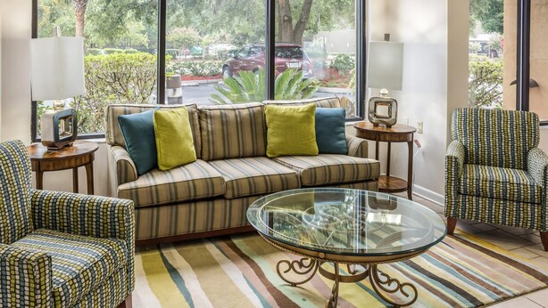 Una sala de estar con sofá, sillones, una mesa de centro de vidrio y vistas al exterior a través de amplios ventanales.